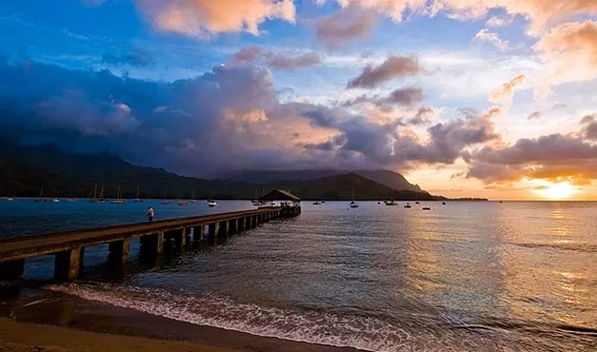 The Hanalei pier at sunset, with Hanalei Bay and the mountains beyond.