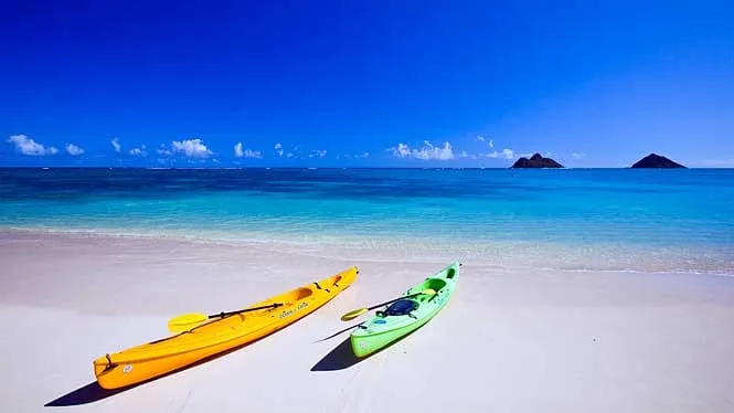 Kayaks on the white sand of Lanikai Beach with the Mokulua islands offshore.