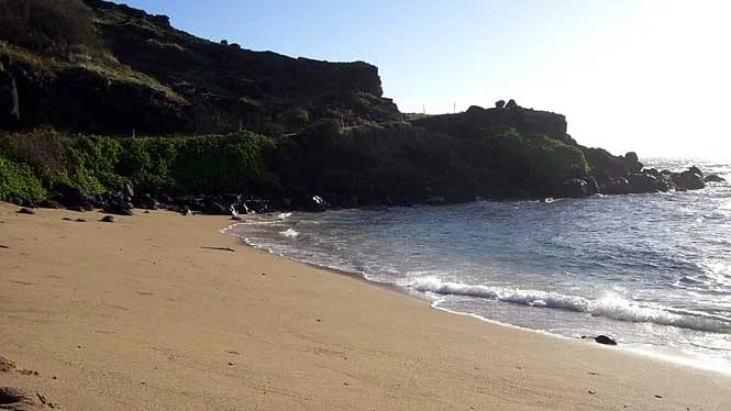 The sandy pocket beach at Honouli Maloo under a dark headland on east Molokai.