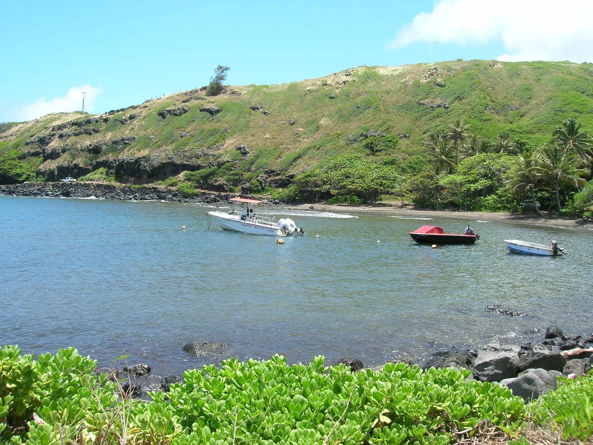 Small boats moored in Honouli Wai bay below the green hills of east Molokai.