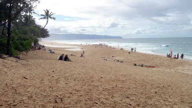 Spectators on the sand at Ehukai Beach Park watching the surf at the Banzai Pipeline.