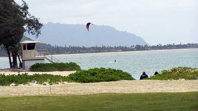 The lifeguard tower and lawn at Kailua Beach Park, with a kitesurfer offshore and the Mokapu peninsula behind.