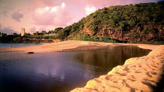 Waimea Bay in evening light, with calm summer water and the jumping rock on the far side.
